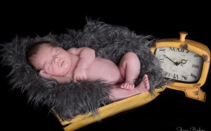 Newborn sleeping in yellow bowl next to clock